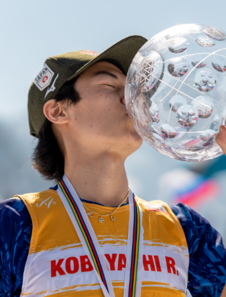 写真：表彰台でメダルを首にかけ、優勝杯にキスをしている小林陵侑